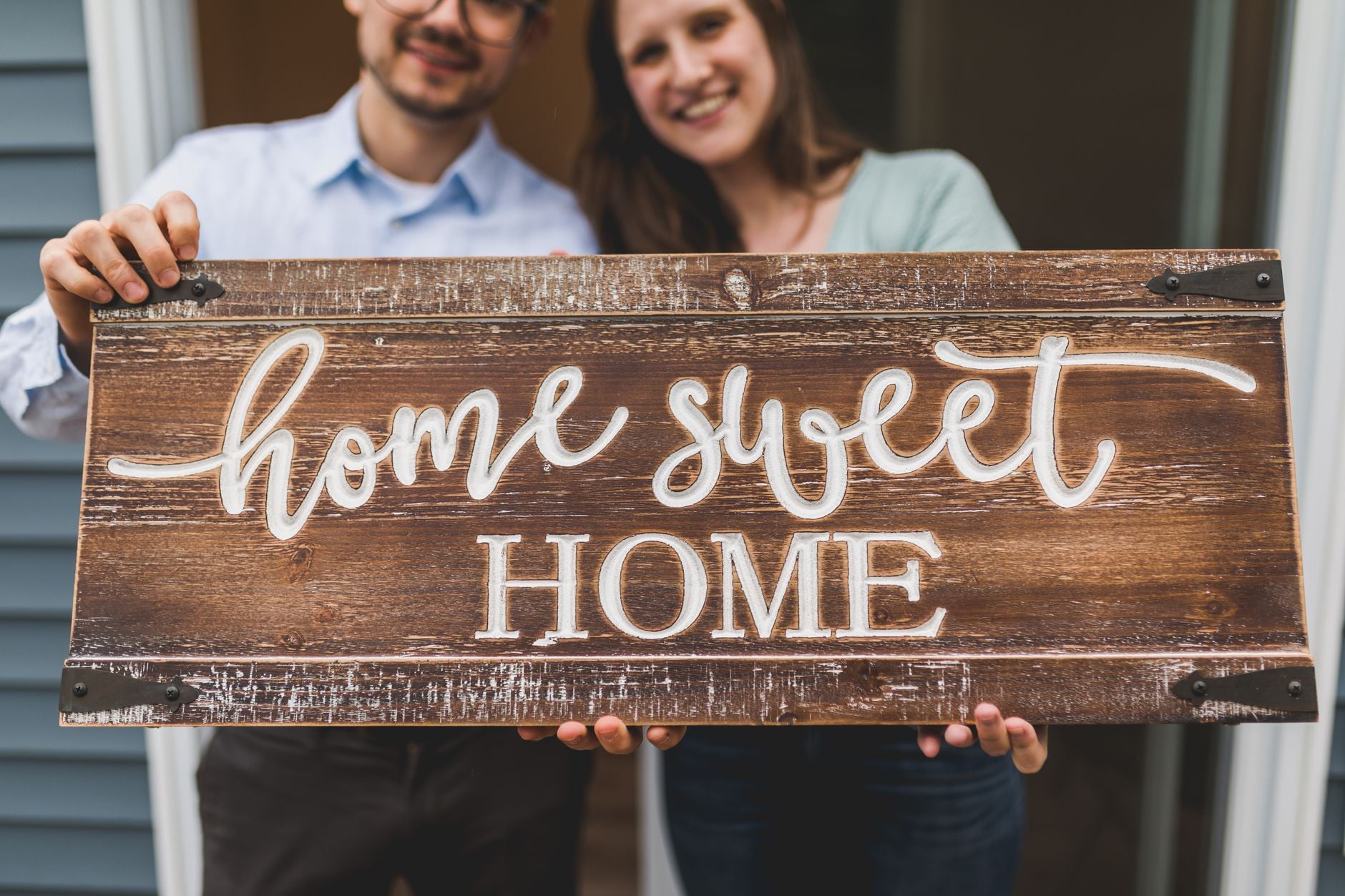 Couple smiling while holding a 'Home Sweet Home' sign, symbolizing new beginnings.
